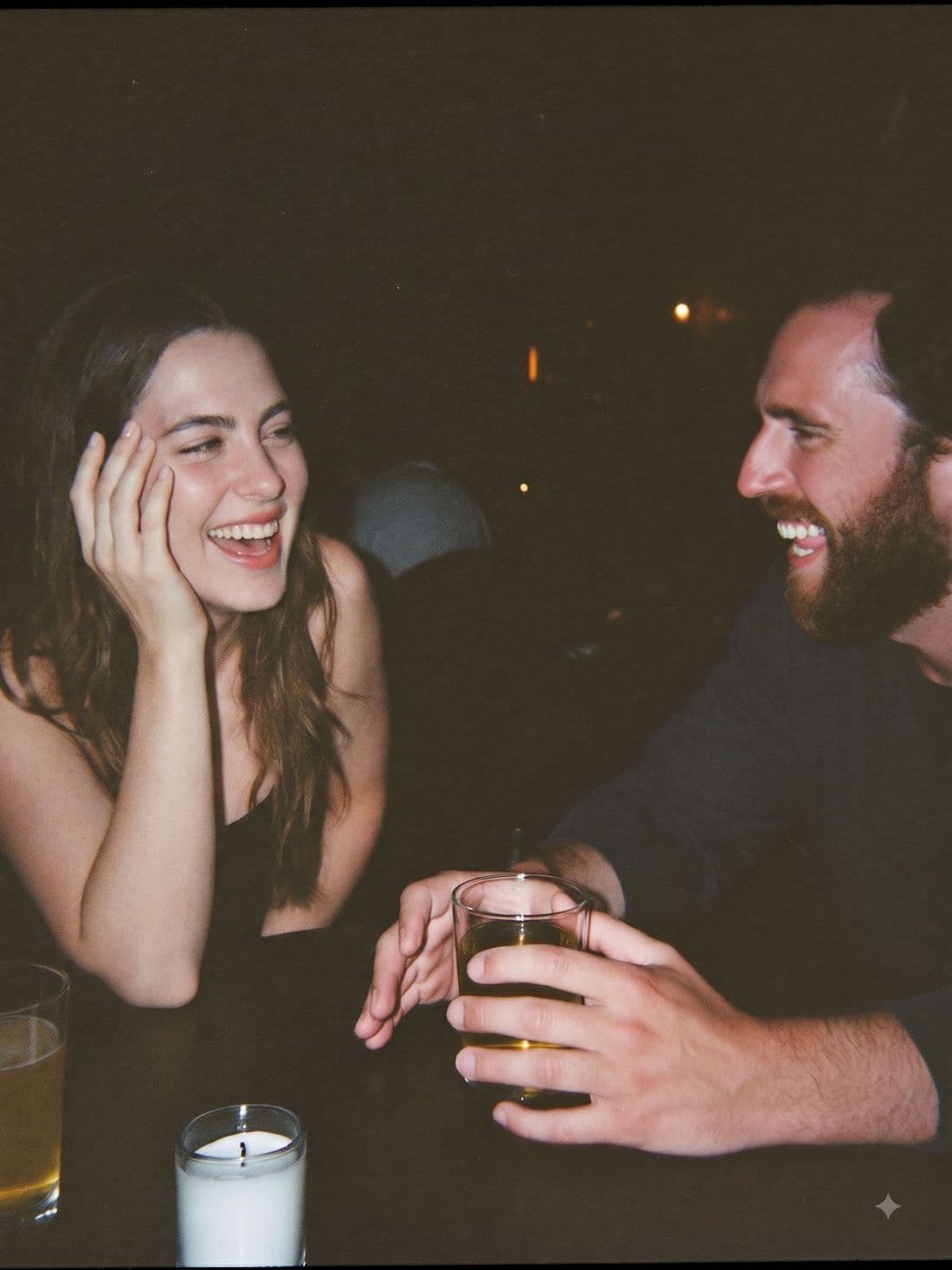 Two people laughing over a drink at a bar