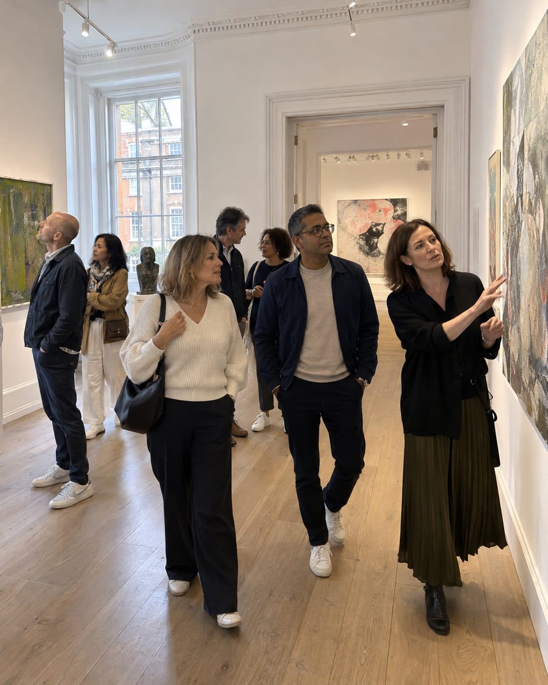 A small group walking through a bright gallery room, one of them pointing out a painting