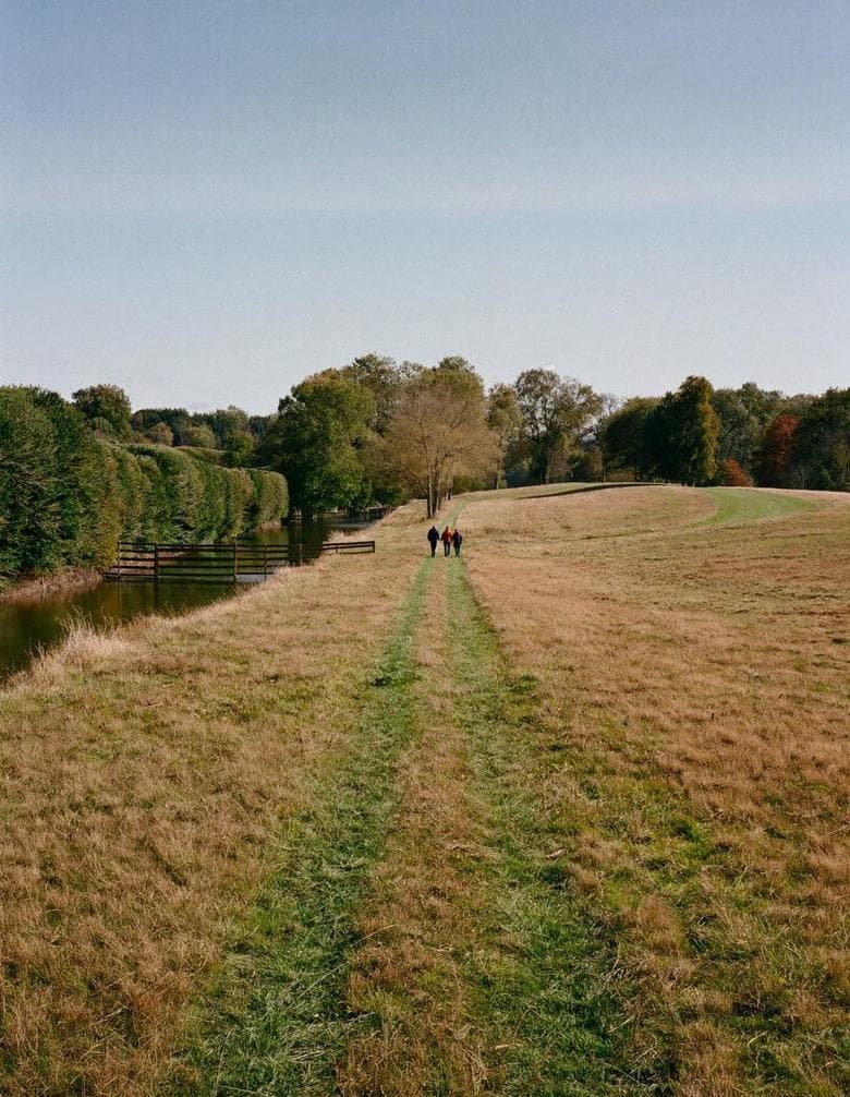A grass path through open fields with walkers in the distance