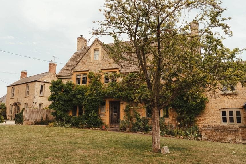 A honey stone Cotswold house behind a lawn and tree