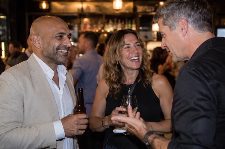 A matched group standing with their drinks at a bar, laughing