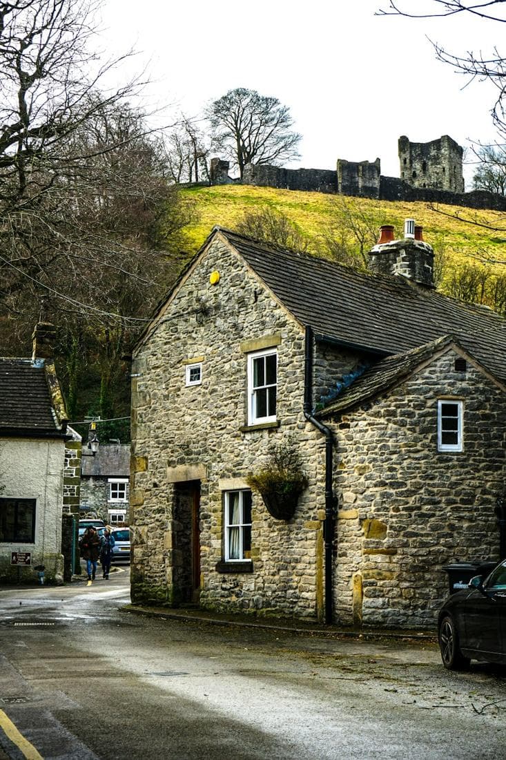 A stone cottage with the ruined keep of Peveril Castle on the hill above