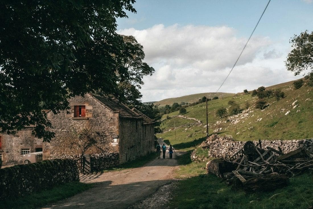 Walkers on a farm lane with green hills rising behind