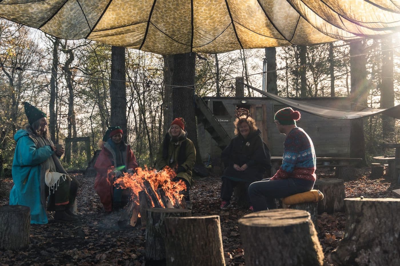 Round the fire in the woods, under the canopy, in winter coats