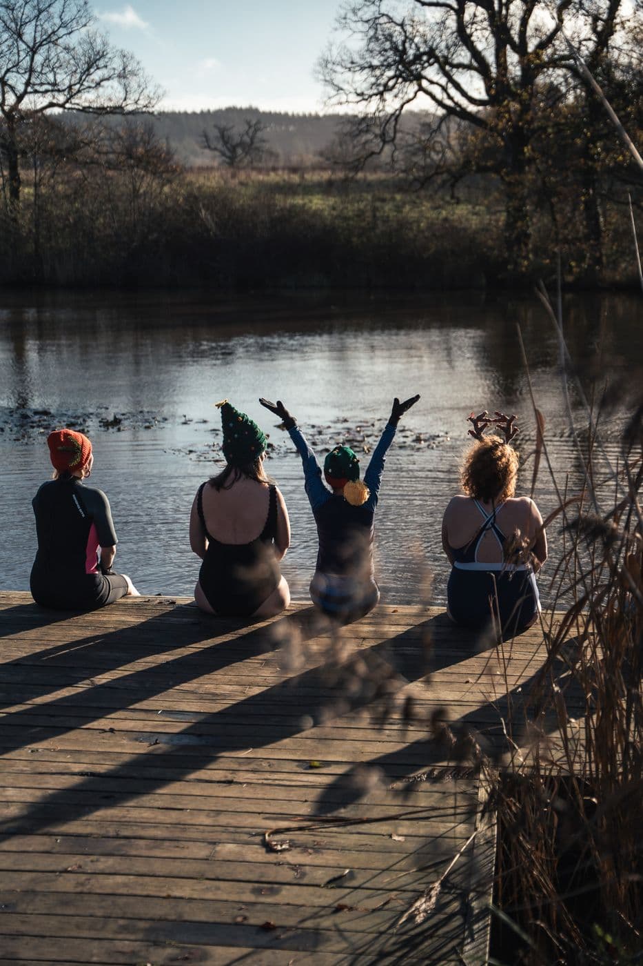 Four people on the jetty by the lake, arms in the air